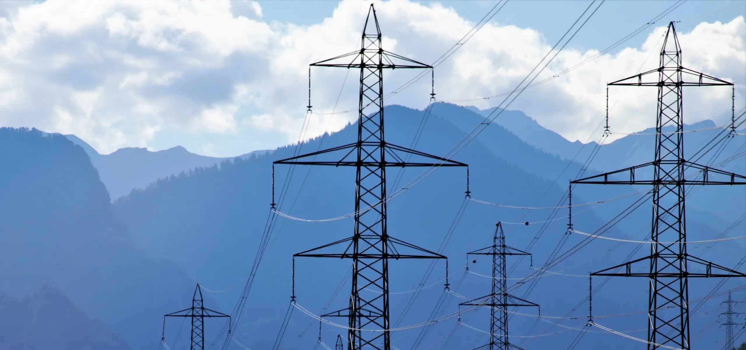 Transmission pylons running across a valley towards a mountain range.
