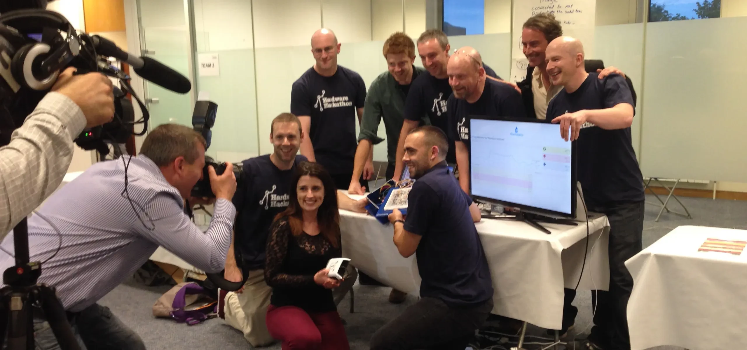 The winning team gathered around a screen at the PCH International hardware hackathon, being filmed.