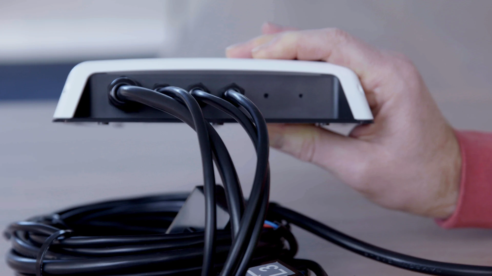 Ein ZEM-Elektrizitätsmonitor, der in einer Hand gehalten wird und dessen Stromsensorleitungen darunter aufgerollt sind.